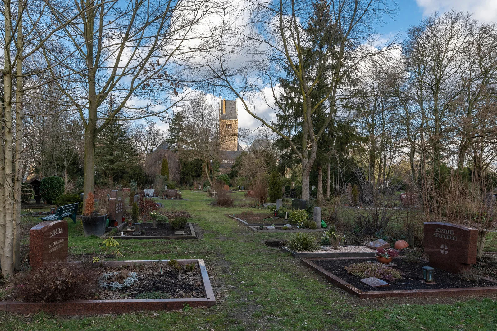 Grabfelder zwischen alten Bäumen mit dem Kapellenturm im Hintergrund auf Südfriedhof Düsseldorf